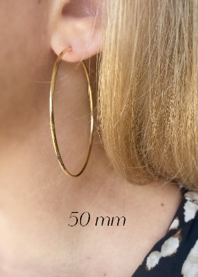 Gold hoop earring worn by a person with visible ear and part of a floral-patterned garment.