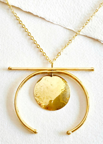 Gold necklace with a circular pendant on a white background
