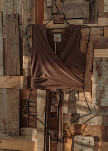 Brown wrap dress on a hanger against a wooden wall.