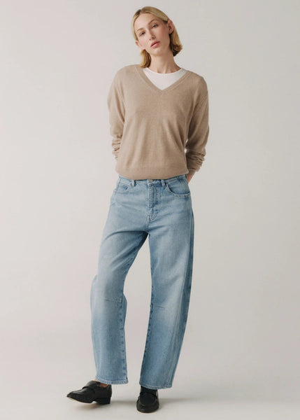 Woman wearing a beige sweater and light blue jeans on a plain background