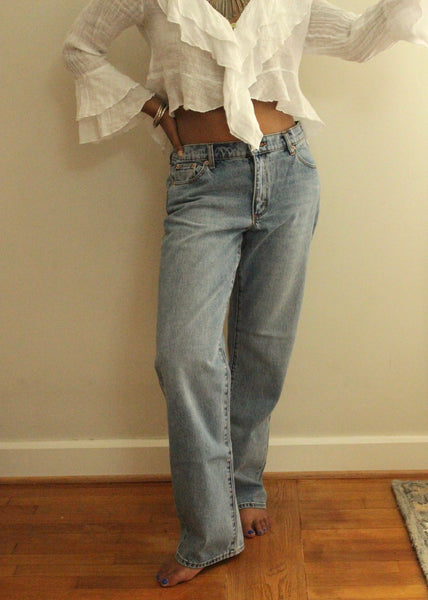 Person wearing a white blouse with ruffled sleeves and high-waisted blue jeans on a wooden floor.