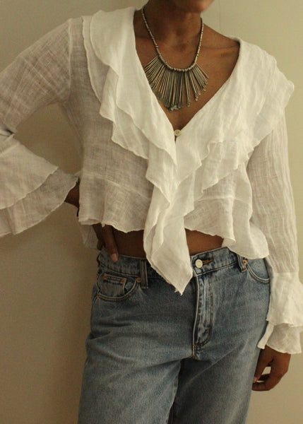 Person wearing a white ruffled blouse and blue jeans against a neutral background