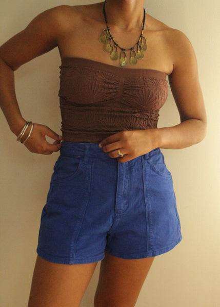 Person wearing a brown strapless top and blue shorts against a plain background