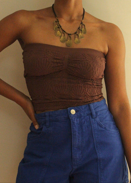 Person wearing a brown strapless top and blue pants with a neutral background
