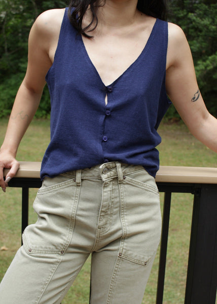 Person wearing a blue sleeveless top and beige pants standing on a wooden deck.