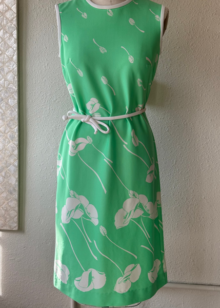 Green dress with white floral pattern on a mannequin against a neutral wall.
