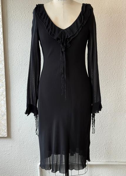 Black dress with sheer sleeves on a mannequin against a textured wall.
