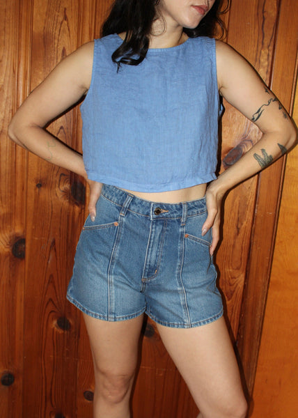 Person wearing a blue sleeveless top and denim shorts against a wooden background