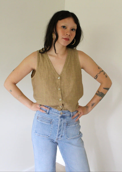 Woman wearing a beige sleeveless top and light blue jeans against a white background