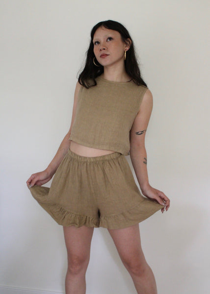 Woman wearing a beige sleeveless top and shorts against a white background