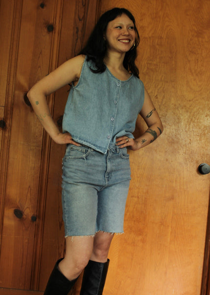 Woman wearing a denim outfit standing against a wooden door.