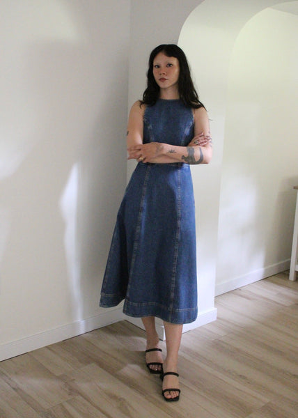 Woman wearing a blue dress standing in a room with white walls and wooden floor.
