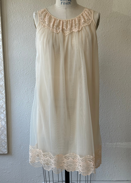 Beige nightgown with lace details on a mannequin against a textured wall.