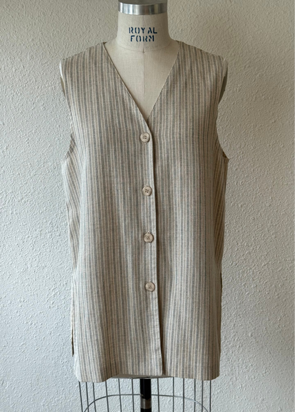 A sleeveless beige and brown vertically striped vest with a V-neck and front buttons, displayed on a dress form against a textured off-white wall.