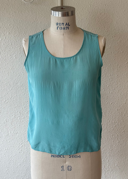 A sleeveless scoop-neck top in a light turquoise blue-green color, displayed on a cream-colored Royal Fern dress form mannequin against a textured off-white wall.