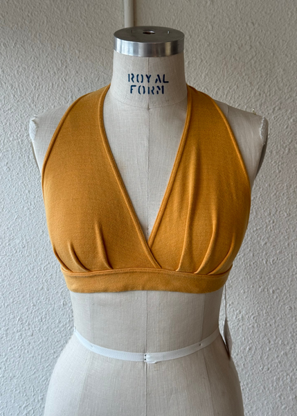 A mustard yellow halter-style wrap top displayed on a cream-colored Royal Form dress form against a textured off-white wall.