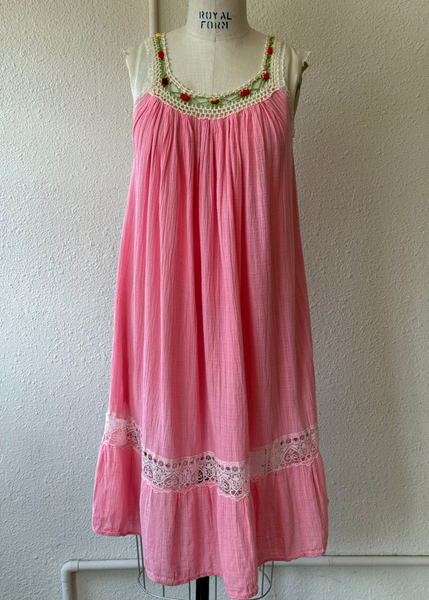 A pink sleeveless cotton nightgown with a floral crocheted neckline and lace hem, displayed on a mannequin torso against a textured off-white wall.