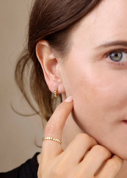 A person wearing gold filled clicker hoop earrings with a textured beaded design.