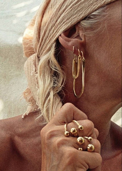 Close-up of a person wearing gold hoop earrings and multiple gold rings.