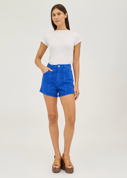 Woman wearing blue shorts and a white top on a plain background